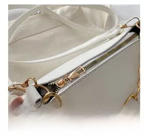 Detailed close-up of the smooth gold metal zipper and chunky chain on a white leather bag
