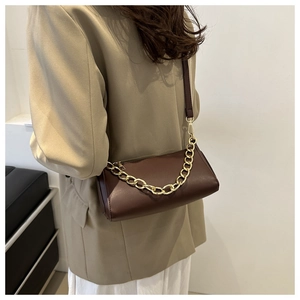 Side view of dark brown cylinder crossbody bag with chunky gold chain on model