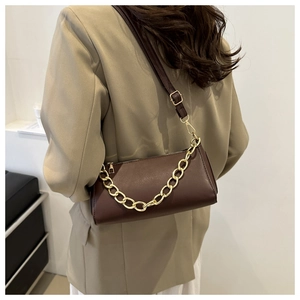 Detail of dark brown leather shoulder bag with gold chain strap on model's beige suit