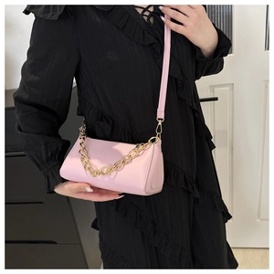 Detail of light pink cylindrical crossbody bag with gold chain strap worn by a model