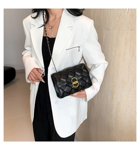 Detail of classic black quilted shoulder bag with gold twist lock on white blazer