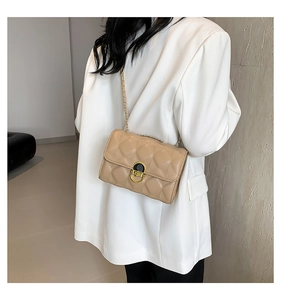 Detailed macro view of beige quilted crossbody bag with golden chain and round metal lock