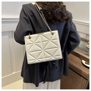 Detail der beige gesteppten Umhängetasche mit goldener Kette an einem Model