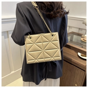 Detailansicht der beigen gesteppten Handtasche mit goldener Kette auf der Schulter