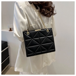 Klassische schwarze Stepptasche mit goldener Kette auf einem weißen Blazer