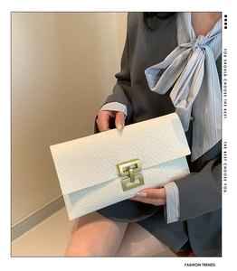 Détail d'une pochette enveloppe blanc cassé avec texture crocodile et boucle dorée chic
