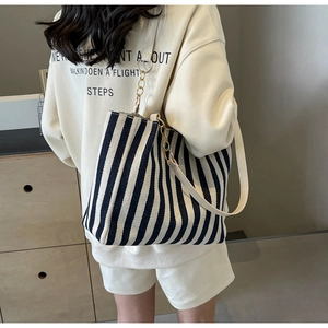 Detail of striped canvas tote bag showing cream leather strap and gold chain accent