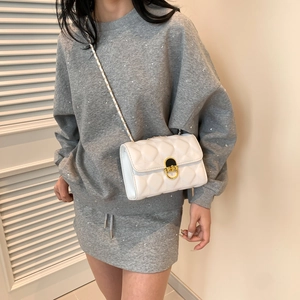 White quilted crossbody bag with gold chain strap shown on a model in a minimal setting