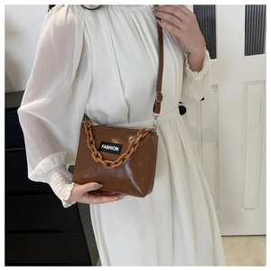 Detail of a brown crossbody bag with decorative orange chain and 'FASHION' label