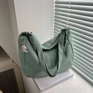Detalle del bolso de pana verde claro con textura suave y un colgante de oveja mona