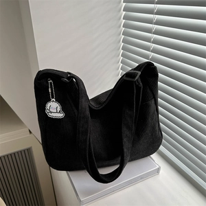 Bolso tote de pana negra con correa ajustable y colgante de perro blanco sobre libros