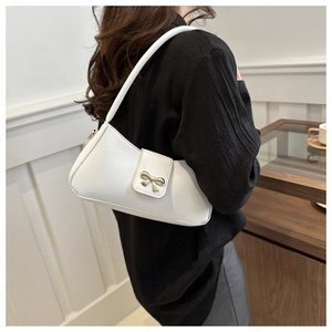 Détail du sac baguette en cuir blanc avec boucle nœud dorée porté à l'épaule du modèle