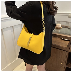 Detail of yellow leather shoulder bag featuring a gold clasp and metal chain strap