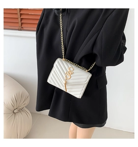 White quilted crossbody bag with gold S-logo and chain strap shown on a model suit