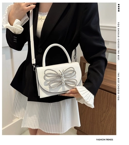 Bolso de cuero blanco con gran hebilla de mariposa de diamantes, lucido por una modelo