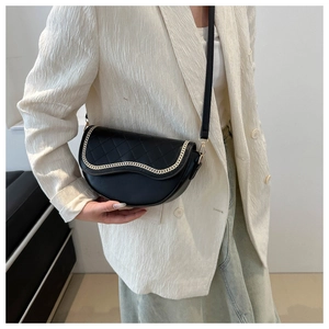 Detalle de bolso silla acolchado negro con cadena dorada sobre blazer blanco