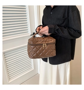 Close-up of brown quilted nylon makeup bag held by a model in a minimal indoor setting