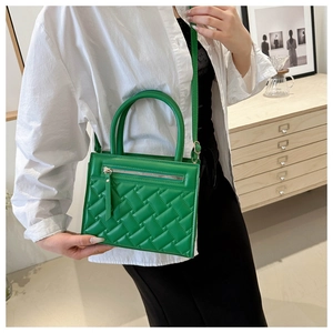 Detail of green quilted handbag with metallic zipper and curved handle on a model