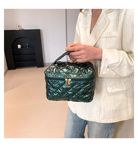 Detail of dark green quilted cosmetic bag with metallic finish and gold zippers