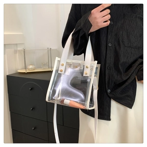 Detail view of transparent PVC beach bag with white leather trim and gold rivet accents