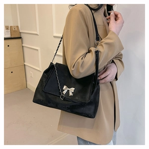 Side view of a black suede crossbody bag featuring a golden butterfly metal buckle charm