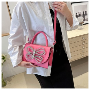 Detalle del bolso bandolera rosa fucsia con una gran mariposa de pedrería en la solapa