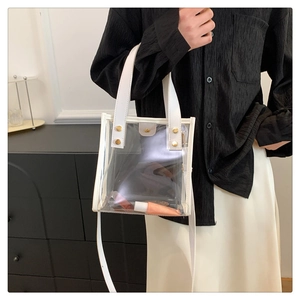Detailed view of clear PVC tote bag with white leather trim and gold metal rivets