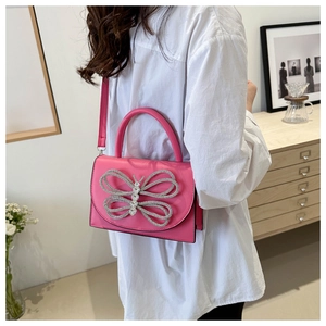 Detalle de bolso rosa con mariposa de strass llevado al hombro sobre una blusa blanca