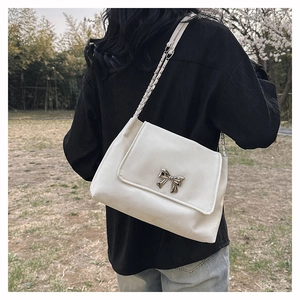 Detail view of cream white PU leather shoulder bag with metallic bow and chain strap
