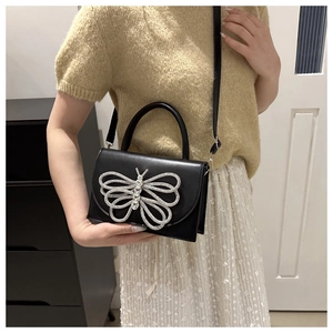 Detalle del gran adorno de mariposa de diamantes en un bolso bandolera de cuero sintético negro