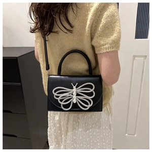 Detalle del bolso bandolera de cuero negro con un adorno de mariposa de strass brillante