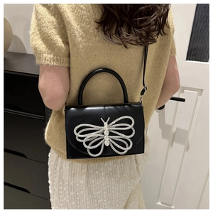 Detalle de bolso bandolera de cuero negro con mariposa de strass en modelo