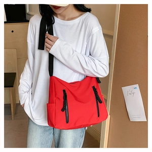 Detail view of a red nylon crossbody bag with black wide strap and vertical zip pockets