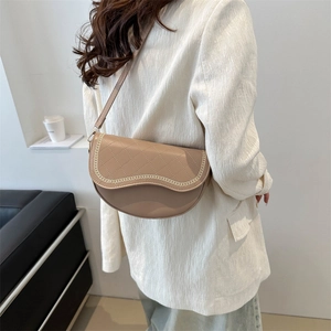 Sac selle matelassé beige avec bordure chaîne et bandoulière porté par un mannequin