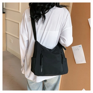 Detail of black nylon tote bag featuring dual front zipper pockets and adjustable strap