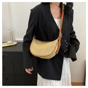 Detail of straw woven crescent bag with brown leather strap and gold buckle on a model