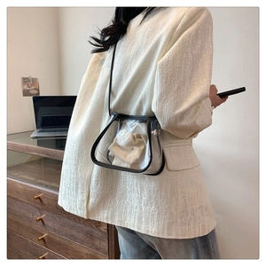 Side view of a transparent crossbody bag with black trim and a beige drawstring pouch