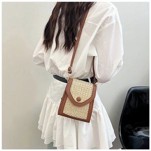 Detail shot of mini woven straw bag with brown leather trim worn as a crossbody