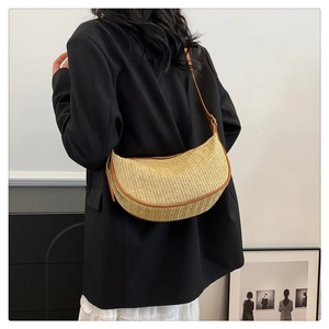 Close-up of a striped woven dumpling bag with leather strap on a model wearing a suit