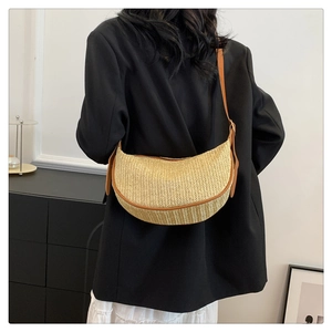 Detail of hand-woven straw crossbody bag with brown leather trim on a model