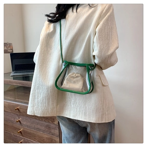 Transparent PVC crossbody bag with green leather trim shown from back on a model