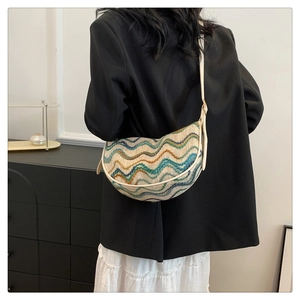 Detail of colorful striped dumpling bag shown as a crossbody on a person in indoor setting