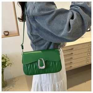 Sac bandoulière vert avec matelassage ondulé et boucle argentée porté par un modèle