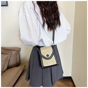 Close-up of woven straw shoulder bag with black trim and long strap on model back