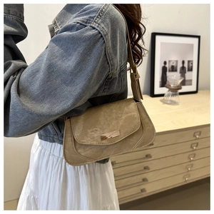 Detail of a beige suede underarm bag with a golden metal buckle shown in a lifestyle setting