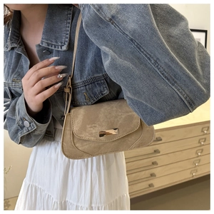 Close-up of khaki suede underarm bag with metal buckle worn by model with denim jacket
