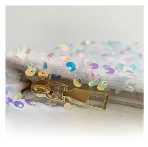 Macro shot of stylish gold metal zipper and iridescent sequins on white plush bag