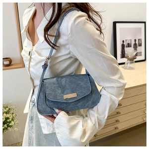 Detail view of blue denim texture bag with metal trim on an indoor lifestyle model