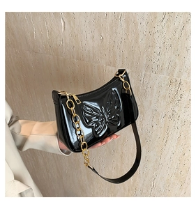 Détail du sac baguette noir verni avec papillon embossé et bandoulière chaîne dorée