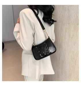Détail du sac sous le bras en cuir verni noir avec gaufrage papillon 3D sur mannequin